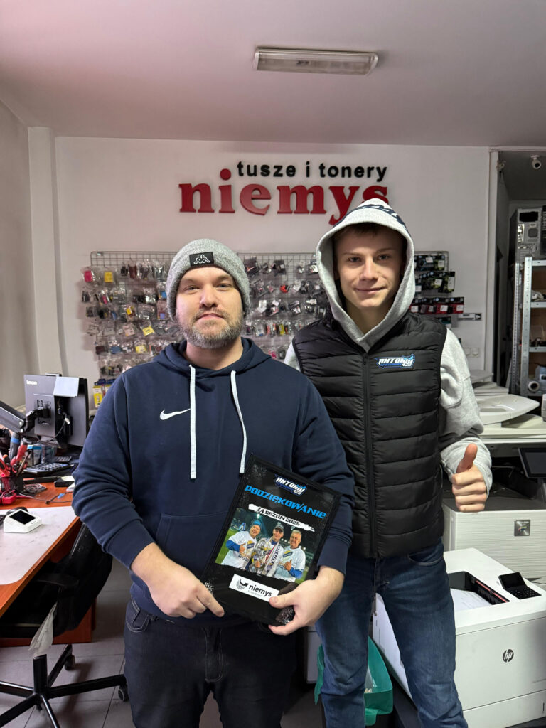 Dwóch mężczyzn stojących w sklepie Niemys, jeden z nich to Antonio Kawczyński – młody żużlowiec trzymający tablicę z podziękowaniem.
