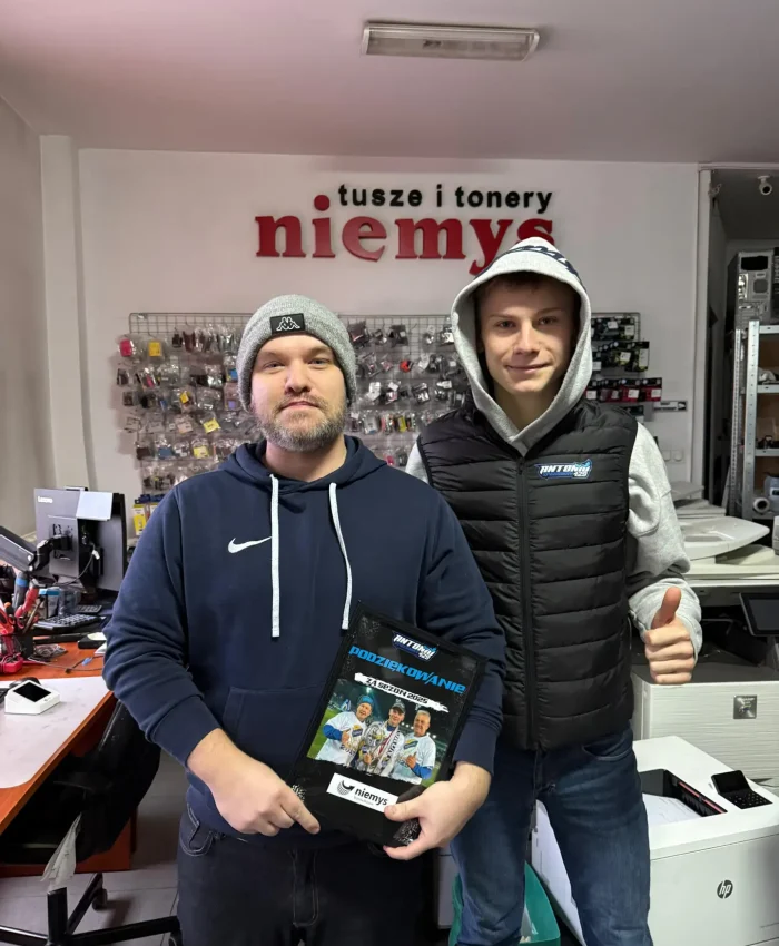 Dwóch mężczyzn stojących w sklepie Niemys, jeden z nich to Antonio Kawczyński – młody żużlowiec trzymający tablicę z podziękowaniem.